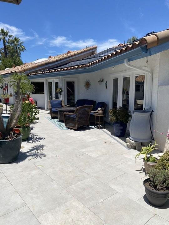 White stucco patio with outdoor seating, potted plants, and a tiled roof under a clear blue sky