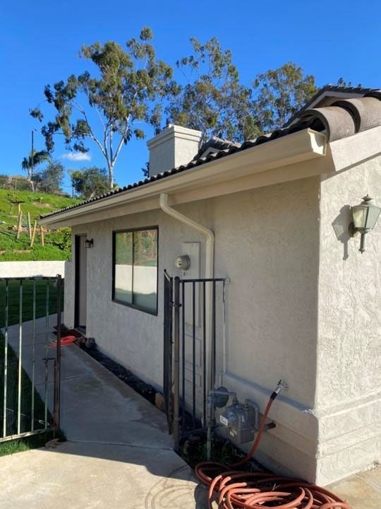 Side of a beige house with a window, outdoor light, and green gate beside a sloped driveway.
