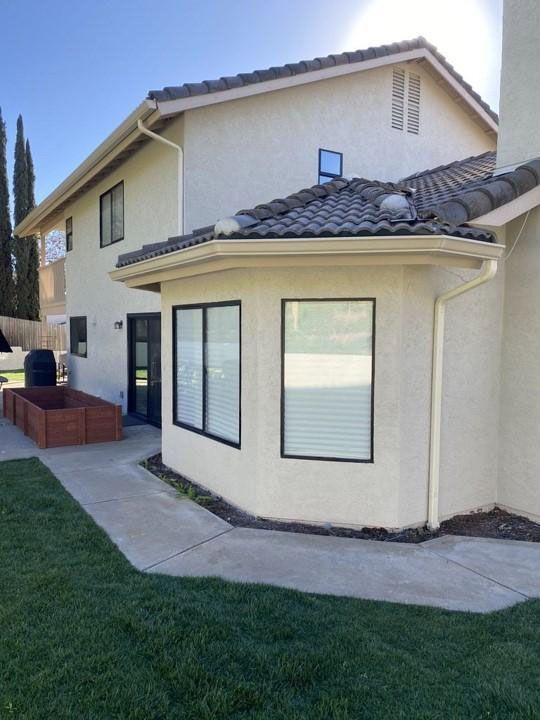 Backyard view of a beige two-story house with a patio, sliding doors, and a grassy lawn