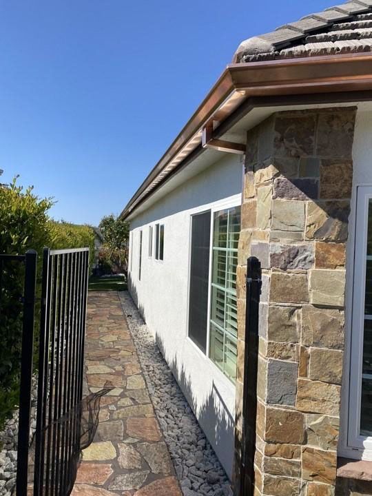 Narrow stone walkway beside a white house with a dark metal fence and blue sky