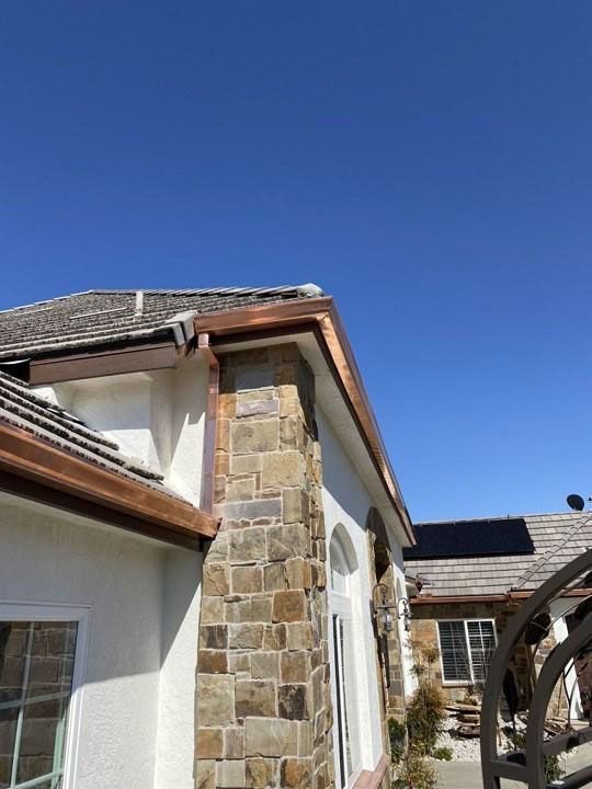 Stone exterior wall and roofline of a house under a clear blue sky, with a covered walkway in front.