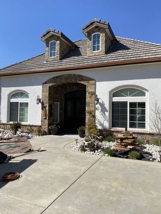 Front view of a stucco house with arched entry, stone trim, and landscaped front walkway