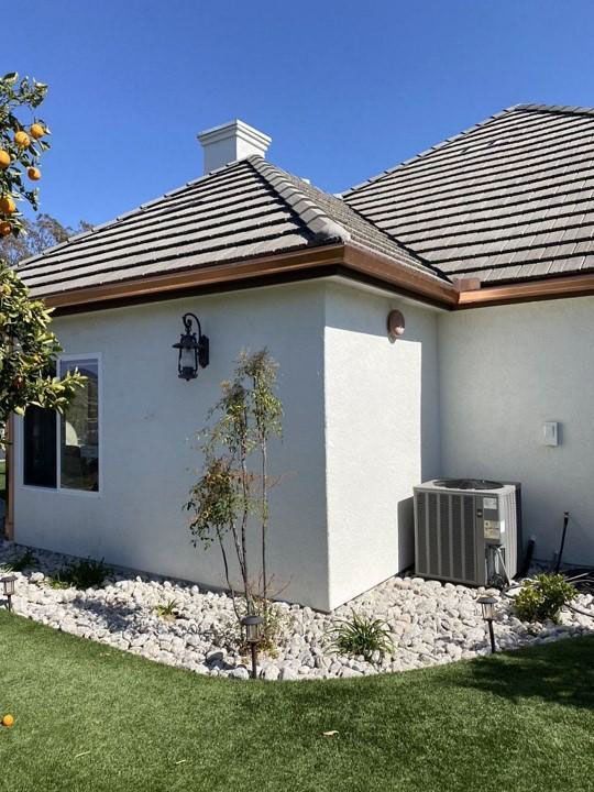 Single-story house exterior with gray roof, white walls, wall lantern, and air-conditioning unit in a landscaped yard