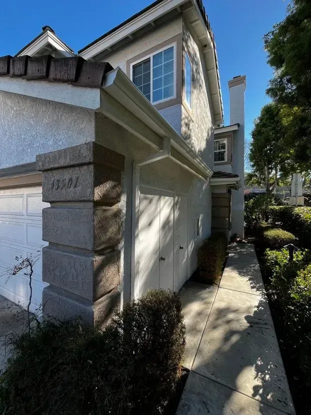 Exterior of a stucco townhouse with a garage, stone trim, and a sunlit walkway along the side.