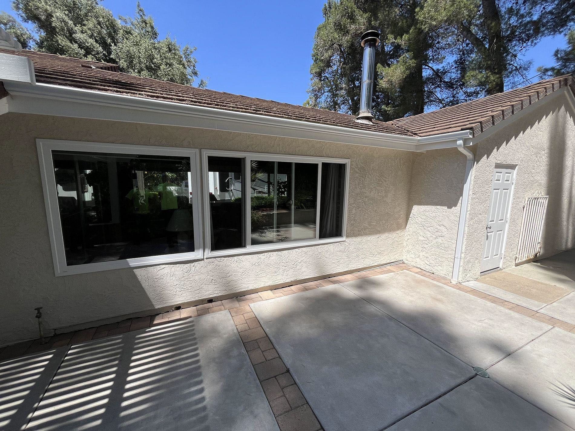 Sunlit stucco courtyard with large windows, tiled roof, and concrete patio with shadow patterns
