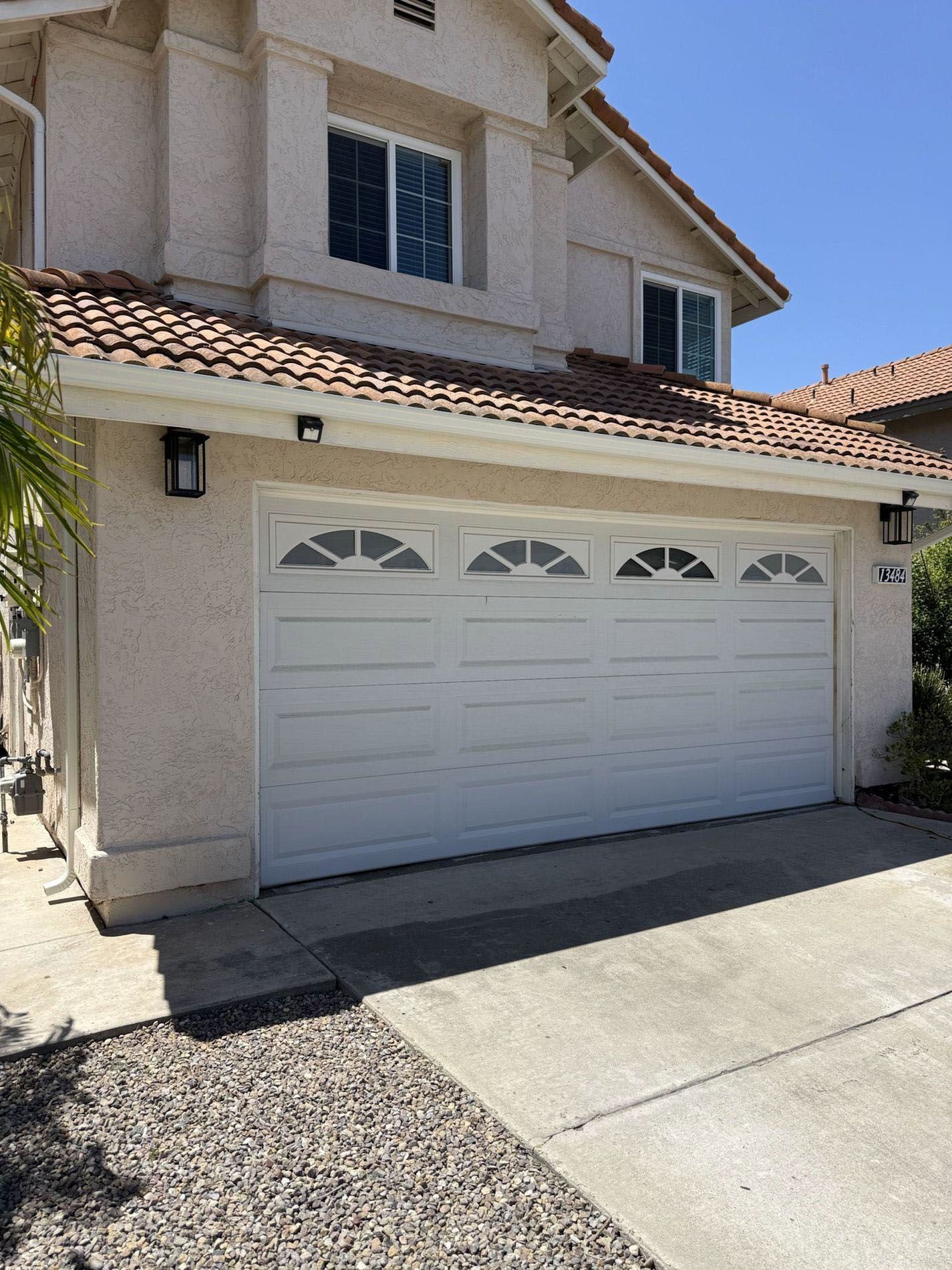 Suburban house exterior with white garage door, stucco walls, and tiled roof in bright sunlight