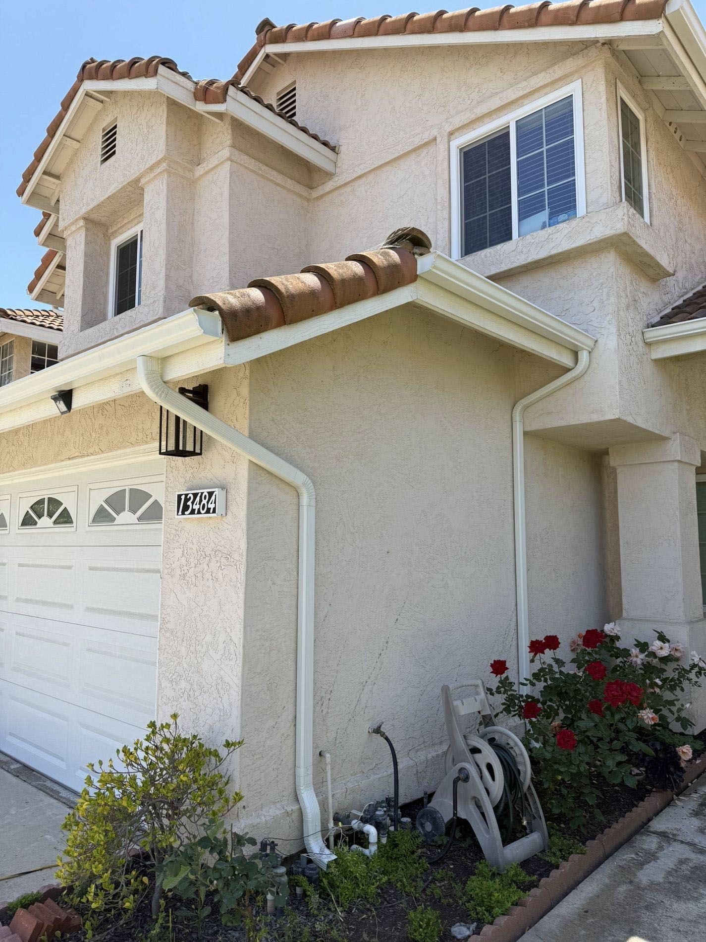 Two-story beige stucco house with white garage door, tiled roof, and bicycles by the front wall.