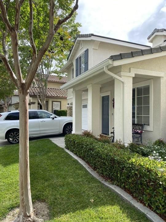 Suburban house with white exterior, trimmed hedges, tree, and a silver car parked in the driveway
