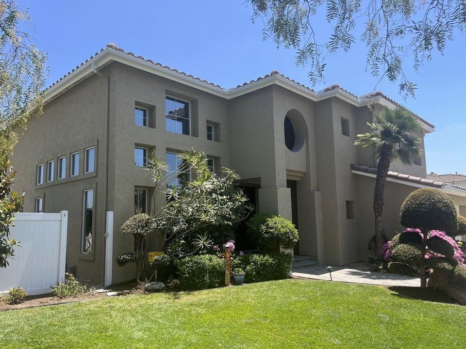 Modern beige two-story house with a manicured lawn and palm trees under a clear blue sky