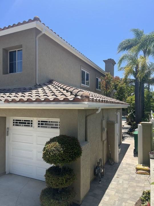 Two-story beige house with white garage door, tiled roof, and palm trees in the driveway.