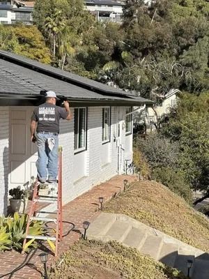 Worker standing on a ladder painting the side of a house beside a steep hillside