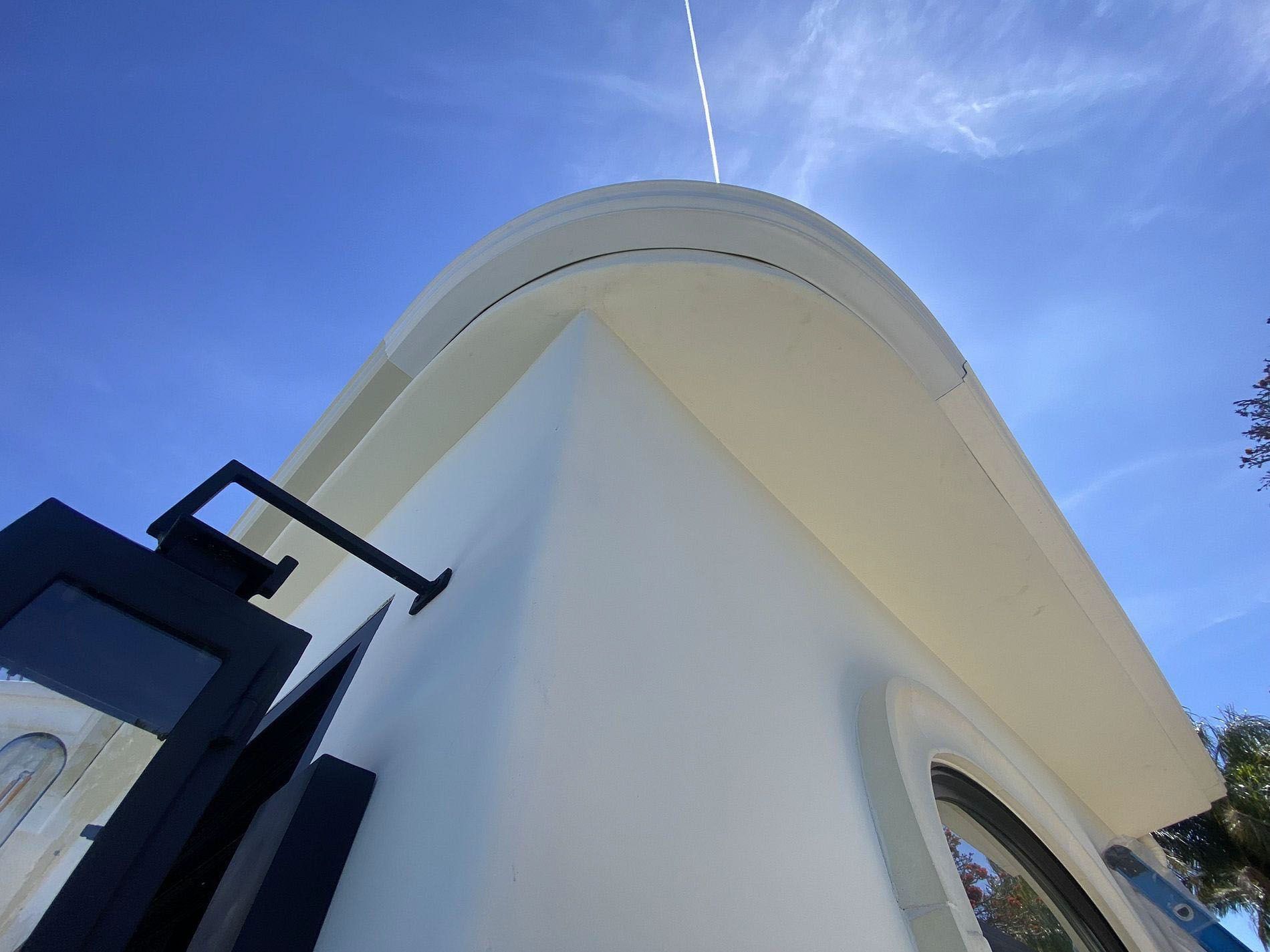 Upward view of a white curved building facade against a blue sky, with a black metal structure on the left.