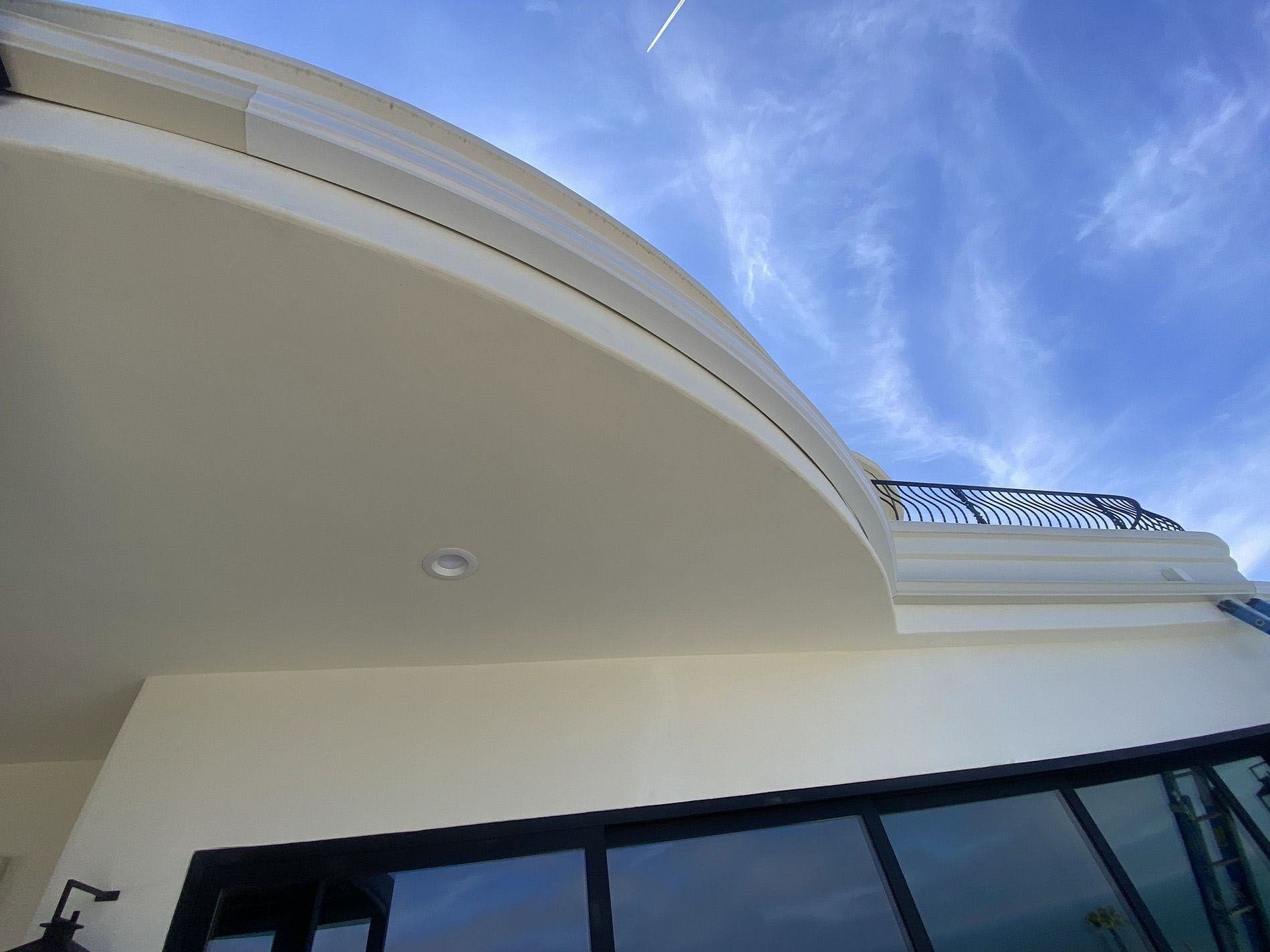 Curved white balcony over dark window frames against a blue sky