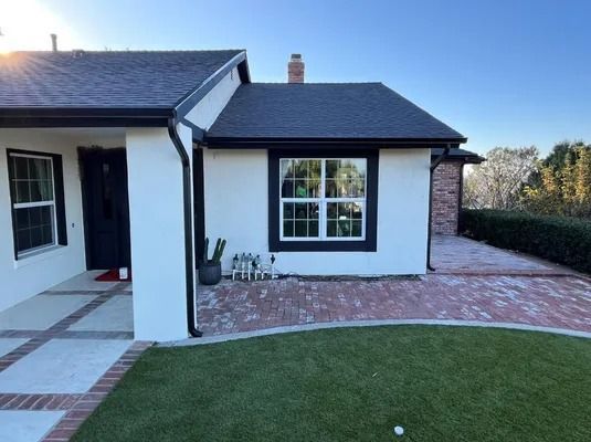 Modern white house exterior with black trim, paved patio, and neatly trimmed lawn