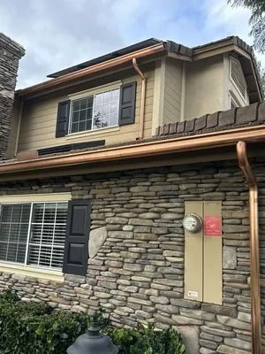 Two-story stone house exterior with brown trim, shutters, and a small hedge in front.