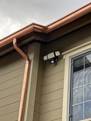 House exterior with copper gutter, tan siding, and a window under the eaves