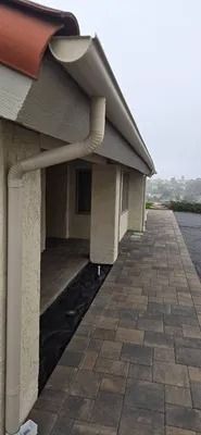 Covered walkway beside a building with tan walls and a paved patio under a cloudy sky