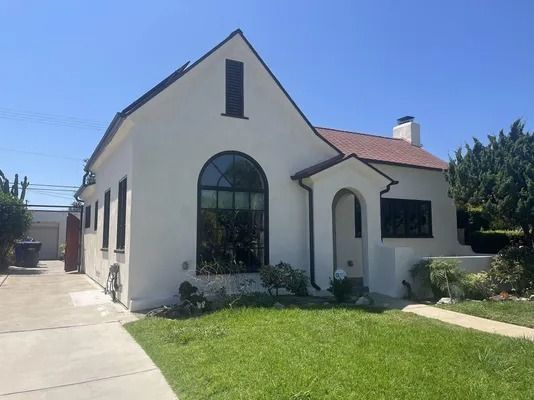 White stucco house with arched windows, red-tiled roof, and a green lawn under a clear blue sky