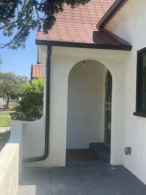 White stucco house entrance with arched doorway, gray tiled porch, and red-tiled roof.
