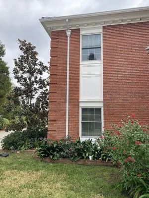 Brick apartment building exterior with white trim, windows, shrubs, and a grassy lawn