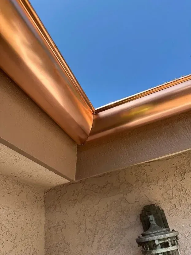 Copper roof eaves framing a blue sky above a stucco wall and outdoor light fixture.