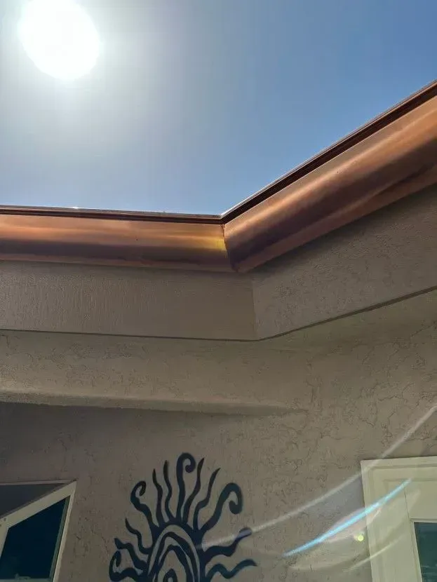 Sunlit patio roof with copper trim and a decorative black wall sculpture below.