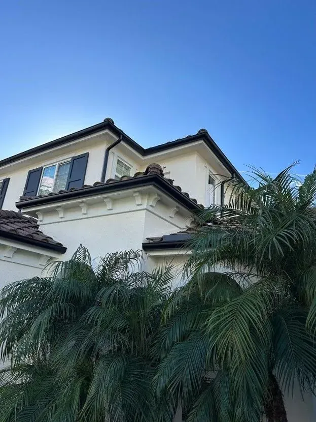 Two-story white house with dark roof and palm trees against a clear blue sky.