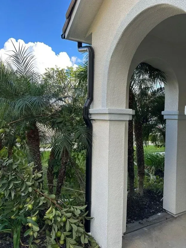 White stucco archway opening to a lush tropical garden with palm trees and greenery.