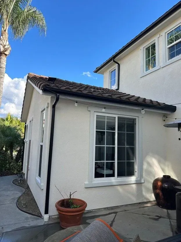 White stucco house exterior with a window, potted plants, and a concrete walkway under a blue sky.