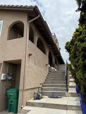 Exterior stairway beside beige apartment building with arched balconies and trash bins