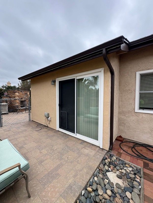 Patio with sliding glass door, tan stucco wall, and stone-tiled floor under a cloudy sky