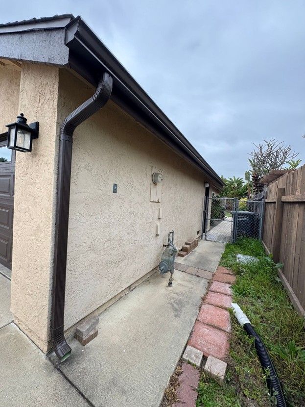 Narrow side yard beside a beige house with a downspout, concrete path, and small utility meter.