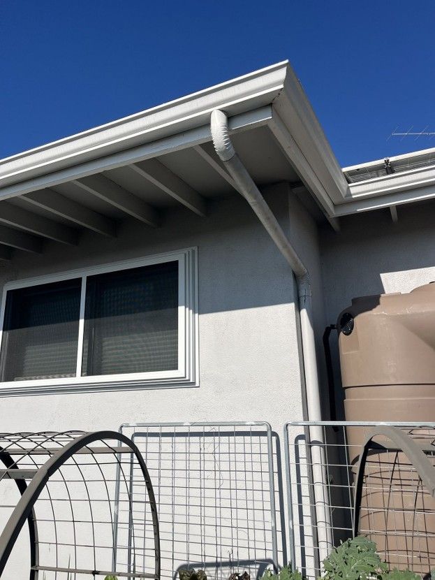 House exterior with white eaves, window, fence, and a tan water tank under a blue sky