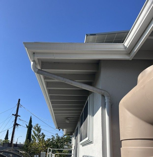 Gray house exterior with white eaves against a clear blue sky, showing rooftop and utility poles nearby
