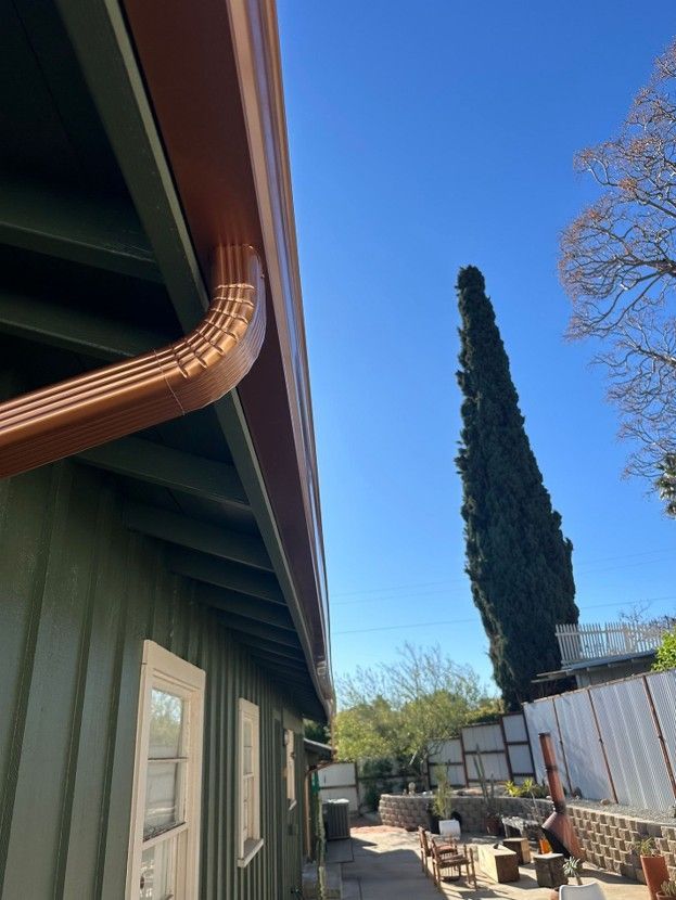 Backyard beside a house with tall cypress tree, blue sky, and patio furniture near a fence