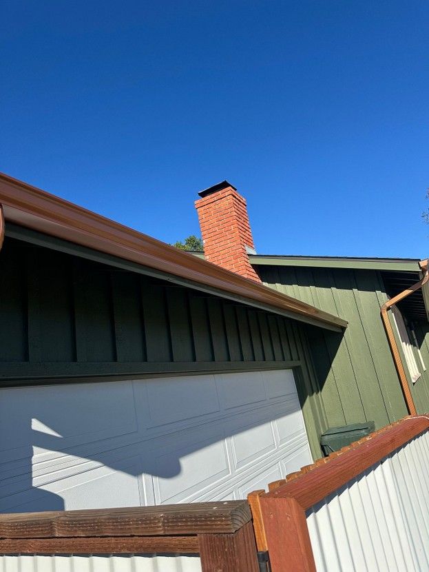 House exterior with green siding, white garage door, brick chimney, and blue sky
