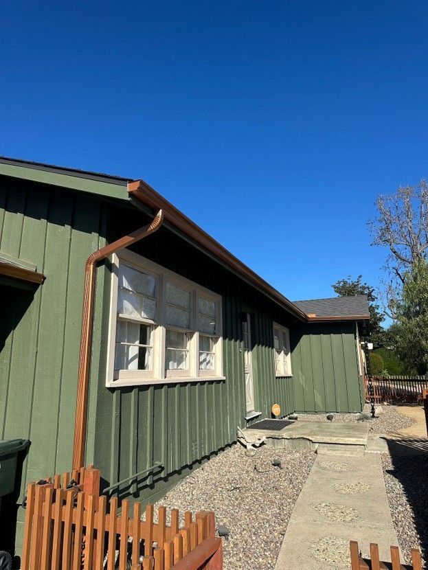 Green house exterior with white-trimmed windows, gravel path, and blue sky