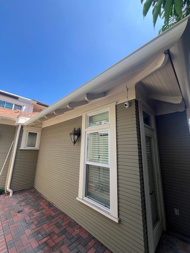 Exterior of beige house with white trim, brick walkway, and a covered side entrance under a blue sky