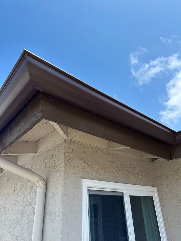House eave and white-framed window beneath a blue sky with a small cloud