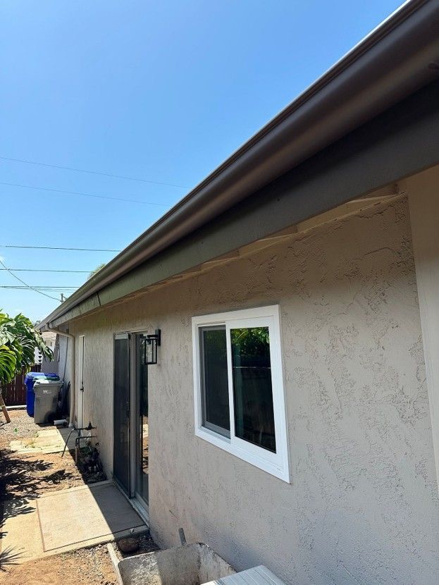 Exterior of a stucco house with a white-framed window, door, and sloped roof under a blue sky