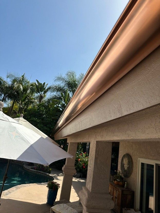 Backyard patio with a large white umbrella, pool, palm trees, and a house roofline under blue sky