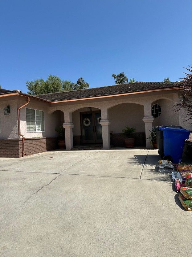 Single-story stucco house with arched porch and a wide concrete driveway on a sunny day
