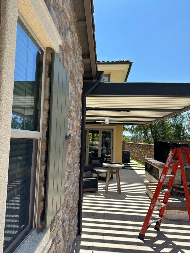 Patio with red ladder, striped awning, and stone house exterior in bright sunlight
