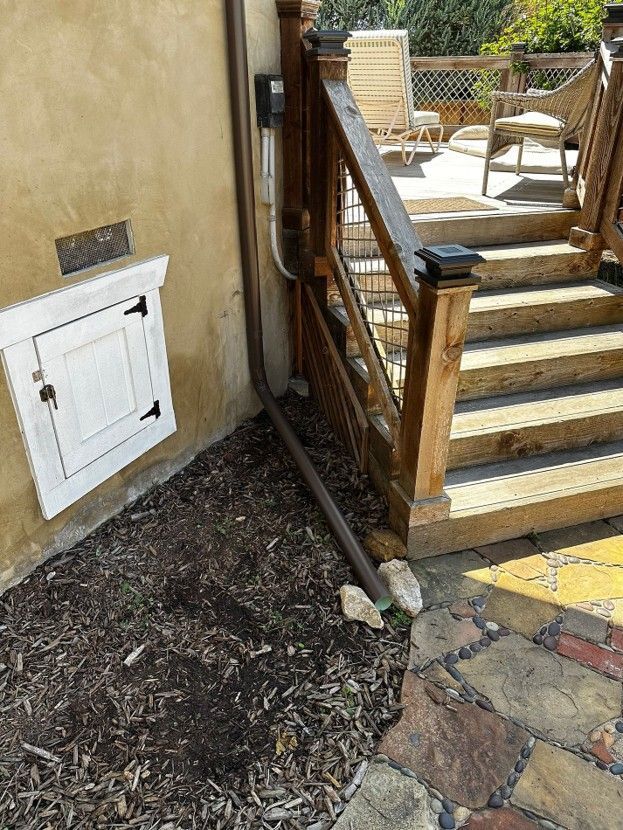Outdoor patio steps with a wooden handrail beside a stucco wall and small white utility door.