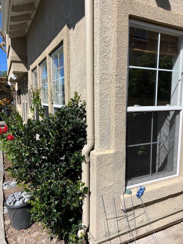 Exterior of a stucco house with windows, shrubs, and a small blue garden ornament by the wall