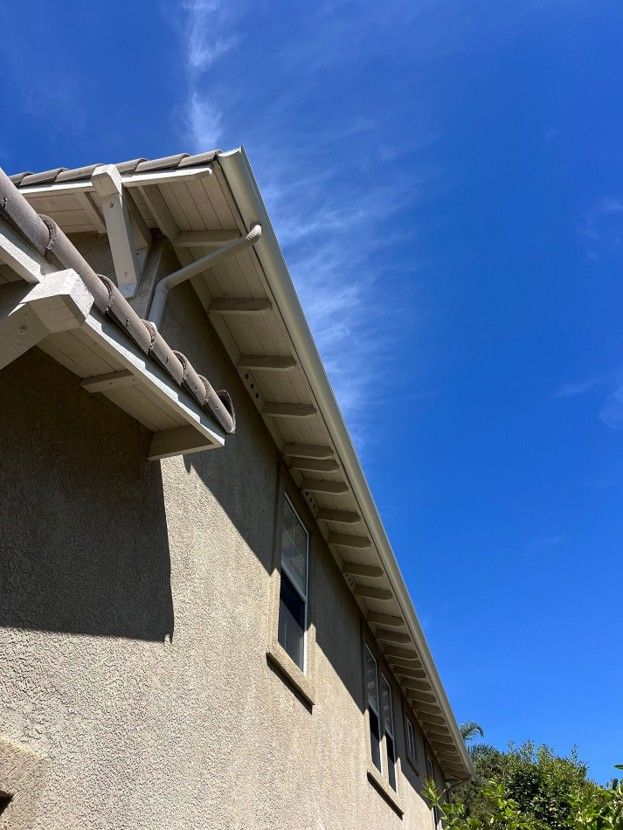 Close-up of a beige house roofline with white gutters against a bright blue sky