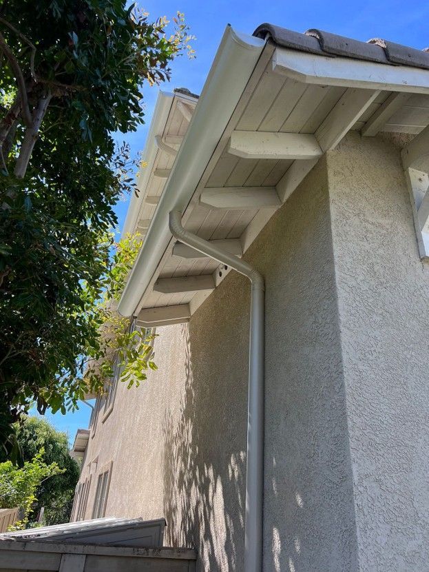 Side view of a beige stucco house with white roof eaves and a tree casting shadows nearby
