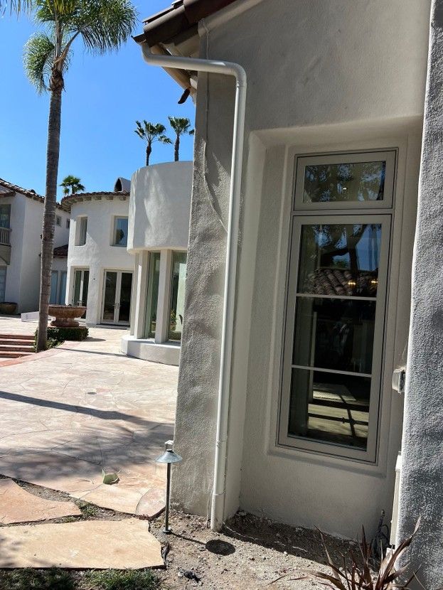 White stucco building exterior with windows, curved awning, and palm trees in a sunny courtyard