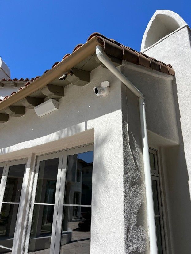White stucco house exterior with brown tile roof, glass doors, and clear blue sky