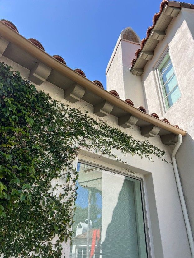 Courtyard view of a white stucco building with ivy, red-tiled eaves, and a large window against a blue sky